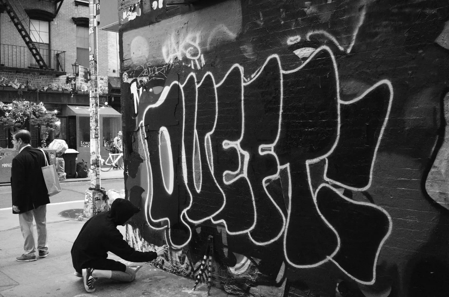 Retocando el graffiti QUEFT mientras pasa un peatón, Nueva York